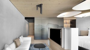 A modern hotel room with a sofa, TV, and a bed.