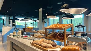 A breakfast buffet with various breads, pastries, and a coffee machine.