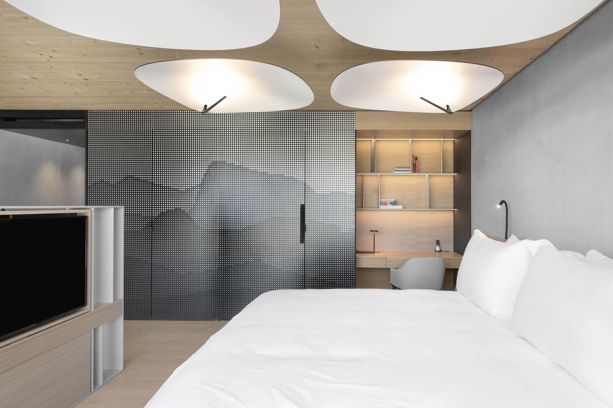 A modern hotel room with a bed, a desk, and a TV.