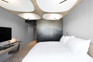 A modern hotel room with a bed, desk, chair, and a large TV.