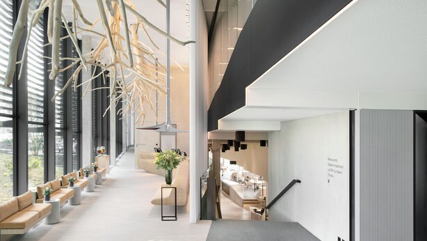 Ein modernes Interieur mit einem langen Korridor, Sitzbereichen und einer Treppe, die zu einem Essbereich führt.