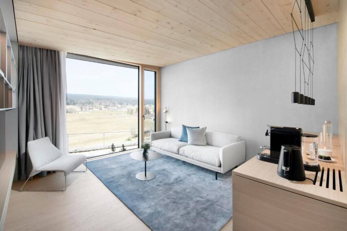 Un salon moderne comprenant un canapé, une table basse, un fauteuil, un bureau avec une machine à café et une vue sur l’extérieur.