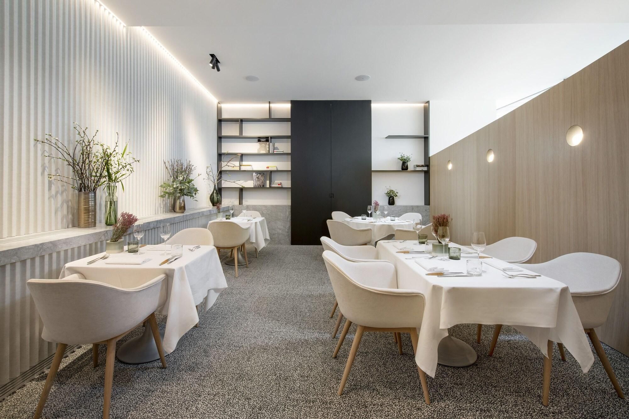 Un espace repas moderne avec des tables et des chaises blanches, un séparateur central noir et des plantes décoratives.