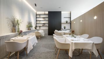 Un espace repas moderne avec des tables et des chaises blanches, un séparateur central noir et des plantes décoratives.