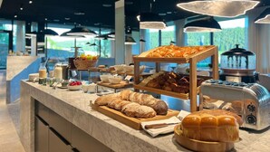 Ein reichhaltiges Frühstücksbuffet mit verschiedenen Brotsorten, Gebäck und einer Kaffeemaschine.
