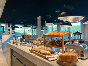 A breakfast buffet with various breads, pastries, and a coffee machine.