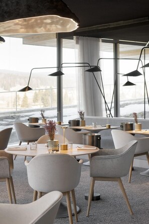 A modern dining area with tables, chairs, and pendant lights. - Hotel Des Horlogers (Le Chenit)