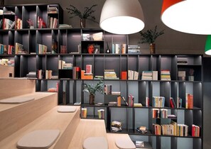 A modern library with tiered bookshelves, a wooden reading area, and pendant lighting. - Hotel Des Horlogers (Le Chenit)