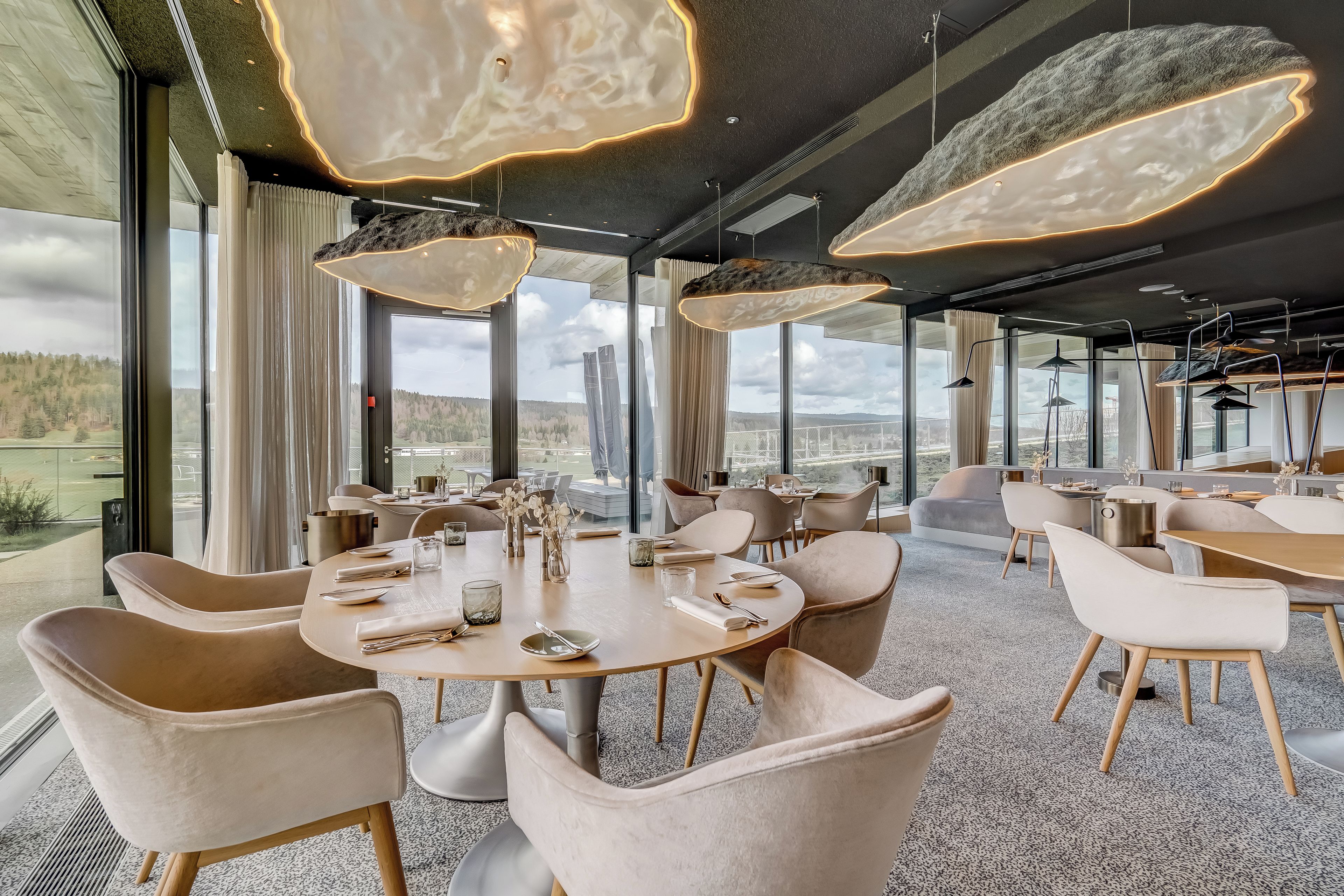 Uma sala de jantar moderna com mesas redondas, cadeiras confortáveis e iluminação pendente.
