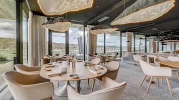 Uma sala de jantar moderna com mesas redondas, cadeiras confortáveis e iluminação pendente.