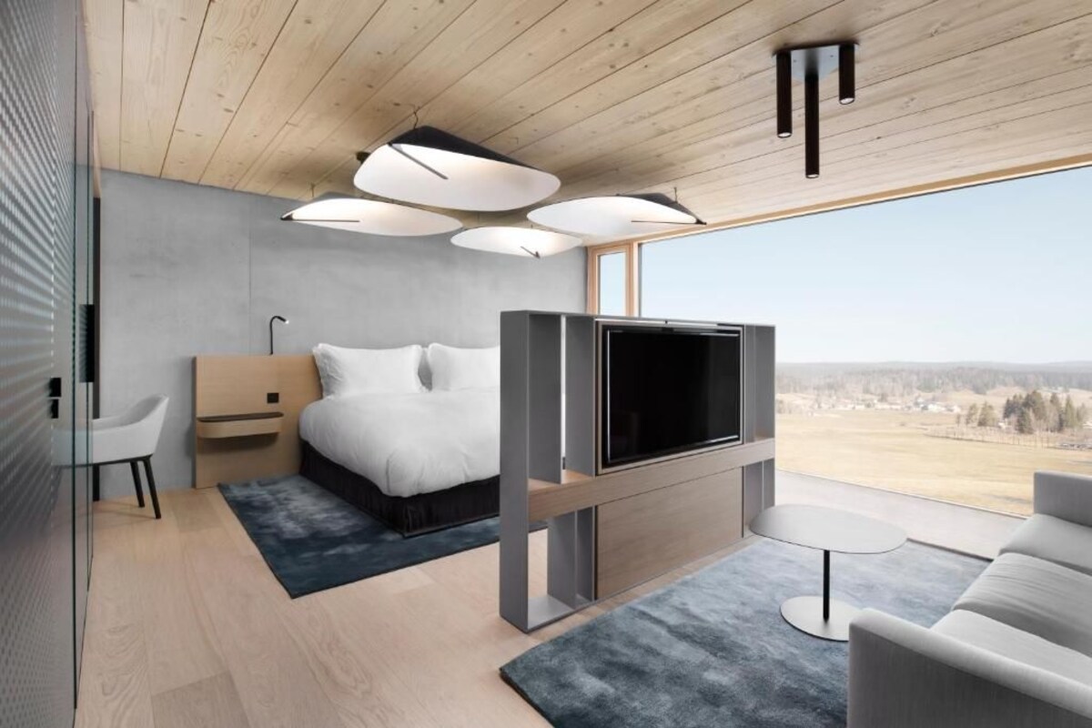 A modern bedroom with a bed, TV, and large windows.