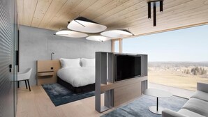 Ein modernes Schlafzimmer mit Bett, Fernseher und großen Fenstern.