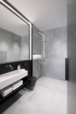 A modern bathroom with a large mirror, a white sink, a black toilet, and a glass-enclosed shower.