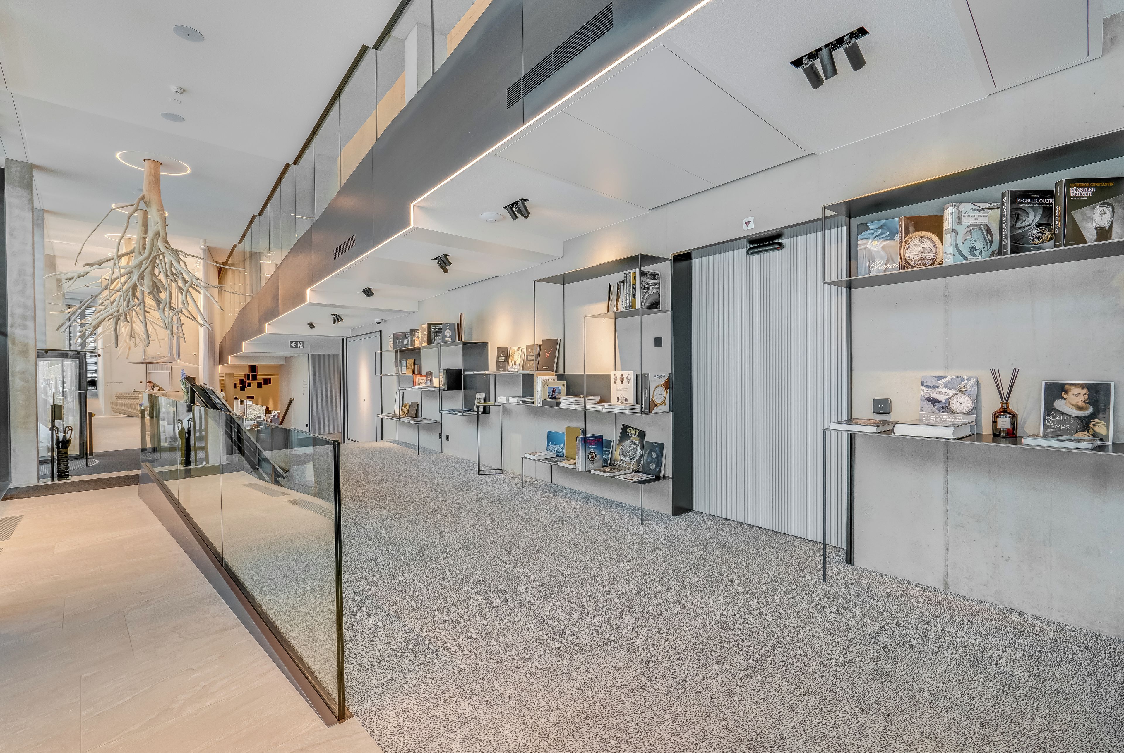 A modern interior with a glass railing, bookshelves, and a unique tree-like light fixture.