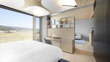 A modern bedroom with a large bed, a desk, a chair, and a view of the outdoors.