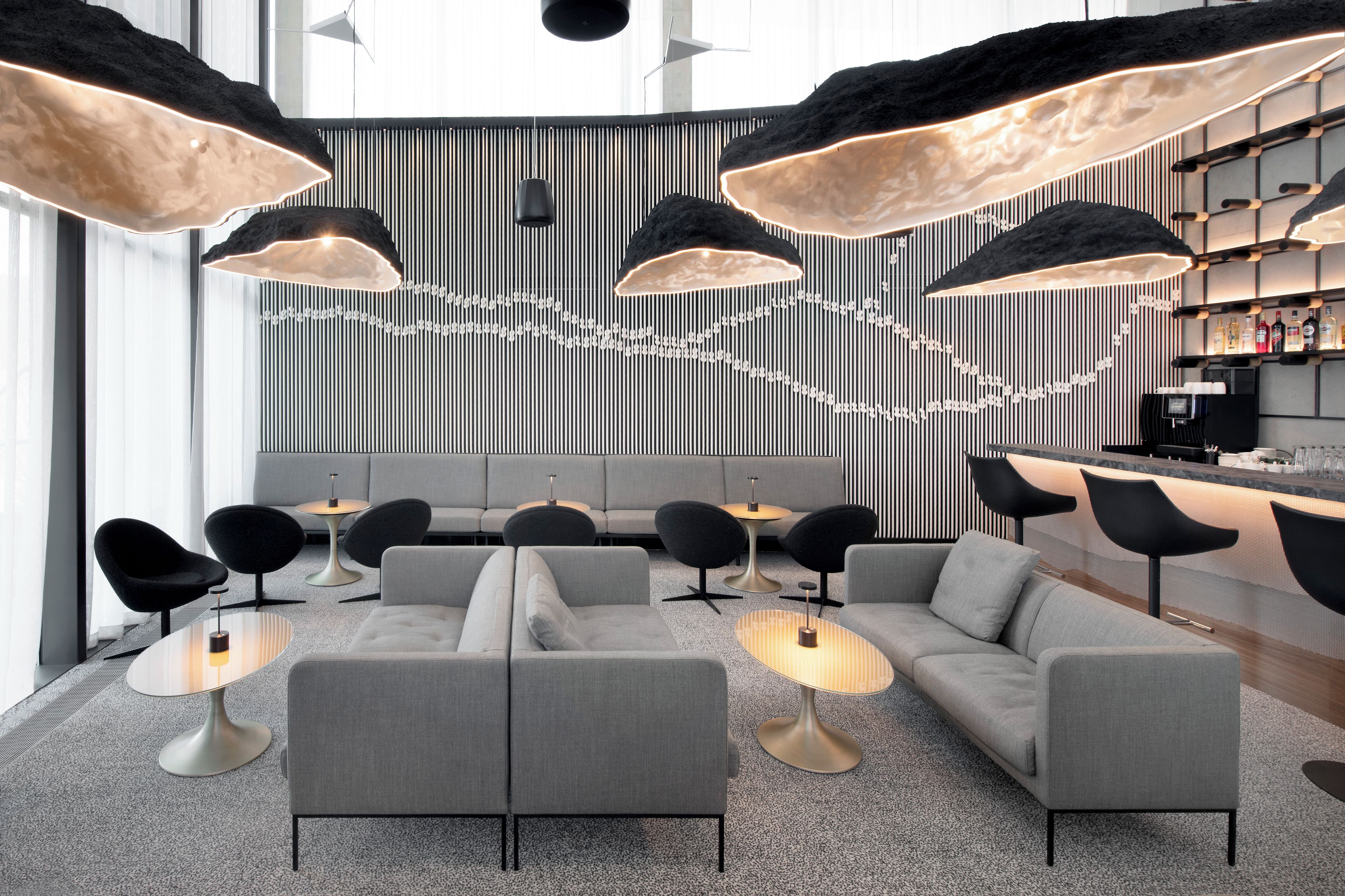 Uma área de estar moderna com sofás, mesas e iluminação pendente.