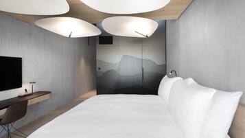 A modern bedroom with a bed, a desk, and a large TV on the wall.