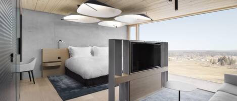 Ein modernes Schlafzimmer mit Bett, Fernseher und Sitzecke, mit großem Fenster und Holzboden.