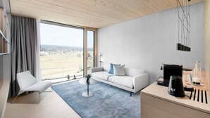 A modern living room with a sofa, a coffee table, a chair, a desk with a coffee machine, and a view of the outdoors.