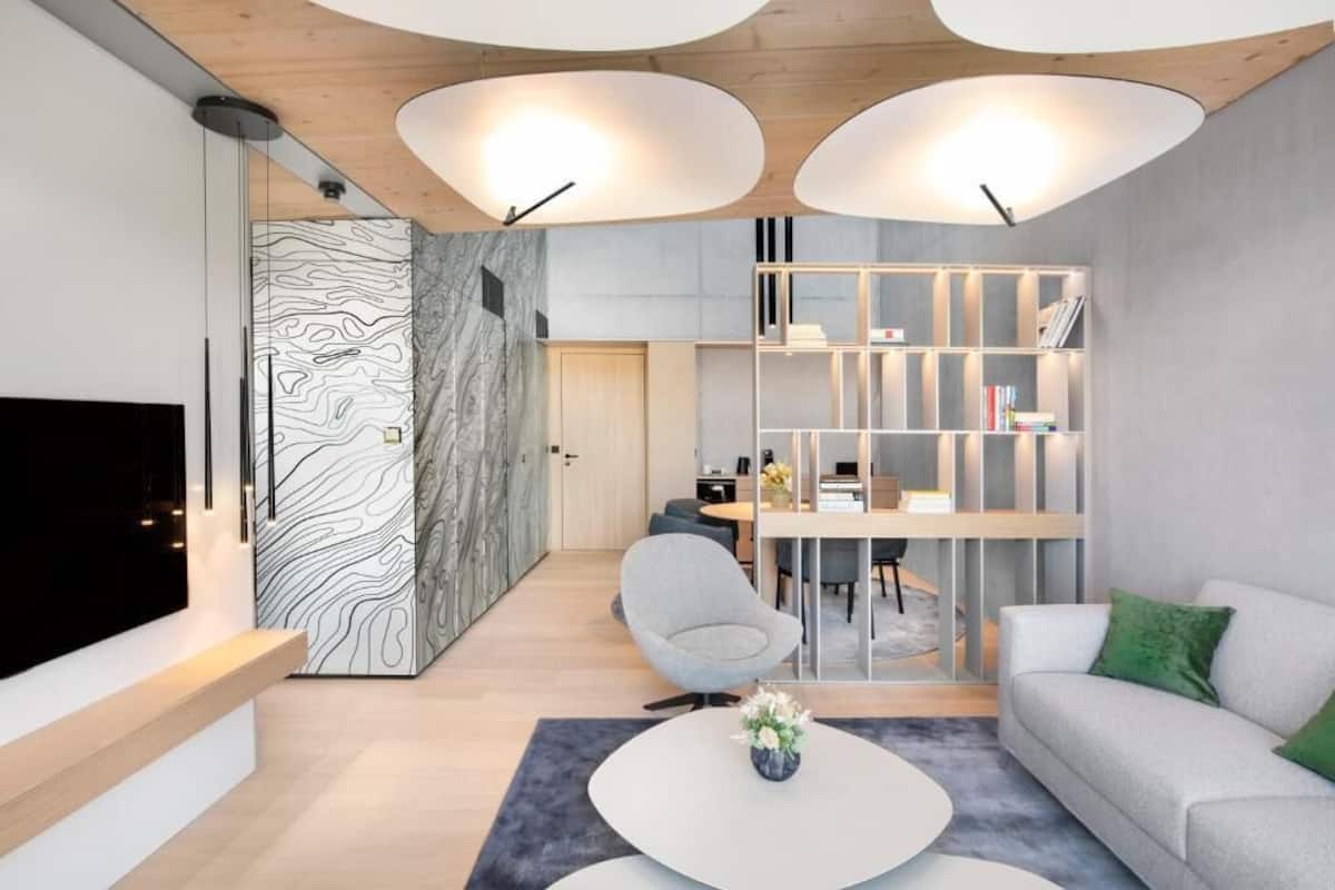 Un salon moderne avec un téléviseur à écran plat, une table basse ronde ornée d’un vase, un canapé gris et une bibliothèque.