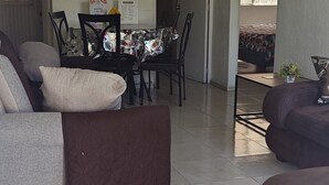 Ein Wohnzimmer mit einer Couch, einem Couchtisch und einem Essbereich mit Stühlen und einem Tisch. Vor dem Eingang liegt eine Willkommensmatte.