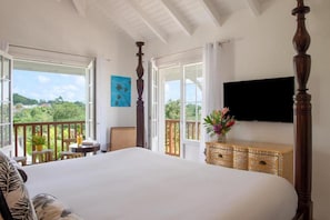 A bedroom with a large bed, a TV mounted on the wall, and a balcony with a view of the greenery.