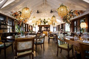 Un restaurante con mesas y sillas de madera, decoraciones florales colgantes y un techo alto con vigas a la vista.