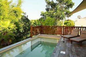 A pool with a wooden deck and lounge chairs, surrounded by lush greenery.