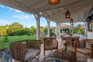 Un patio al aire libre con mobiliario de mimbre, una zona de comedor y vistas a un jardín exuberante.