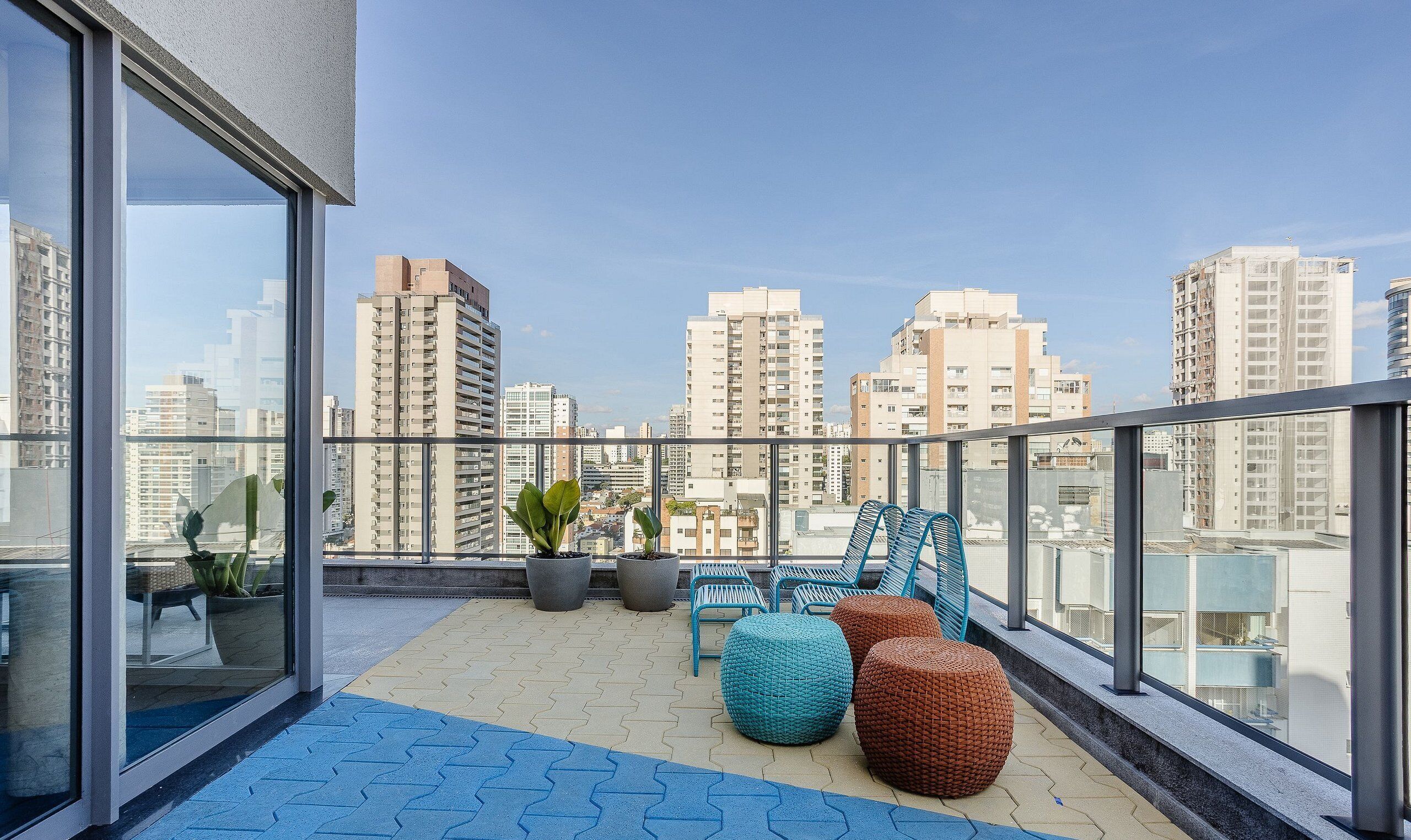 A balcony with potted plants, blue and brown seating, and a city view.