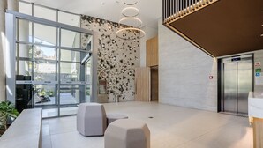 Un vestíbulo moderno con puertas de vidrio, una pared con diseño, un mueble de madera y un panel de control de ascensor digital.