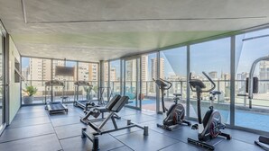 Un gimnasio moderno con diverso equipo de ejercicio, ventanas amplias y vistas de la ciudad.