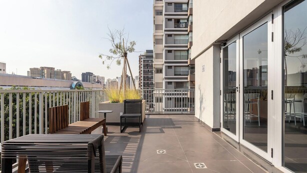 Un balcon extérieur moderne, doté d’un espace salon, offrant une vue sur la ville et donnant sur un immeuble avec des portes vitrées.