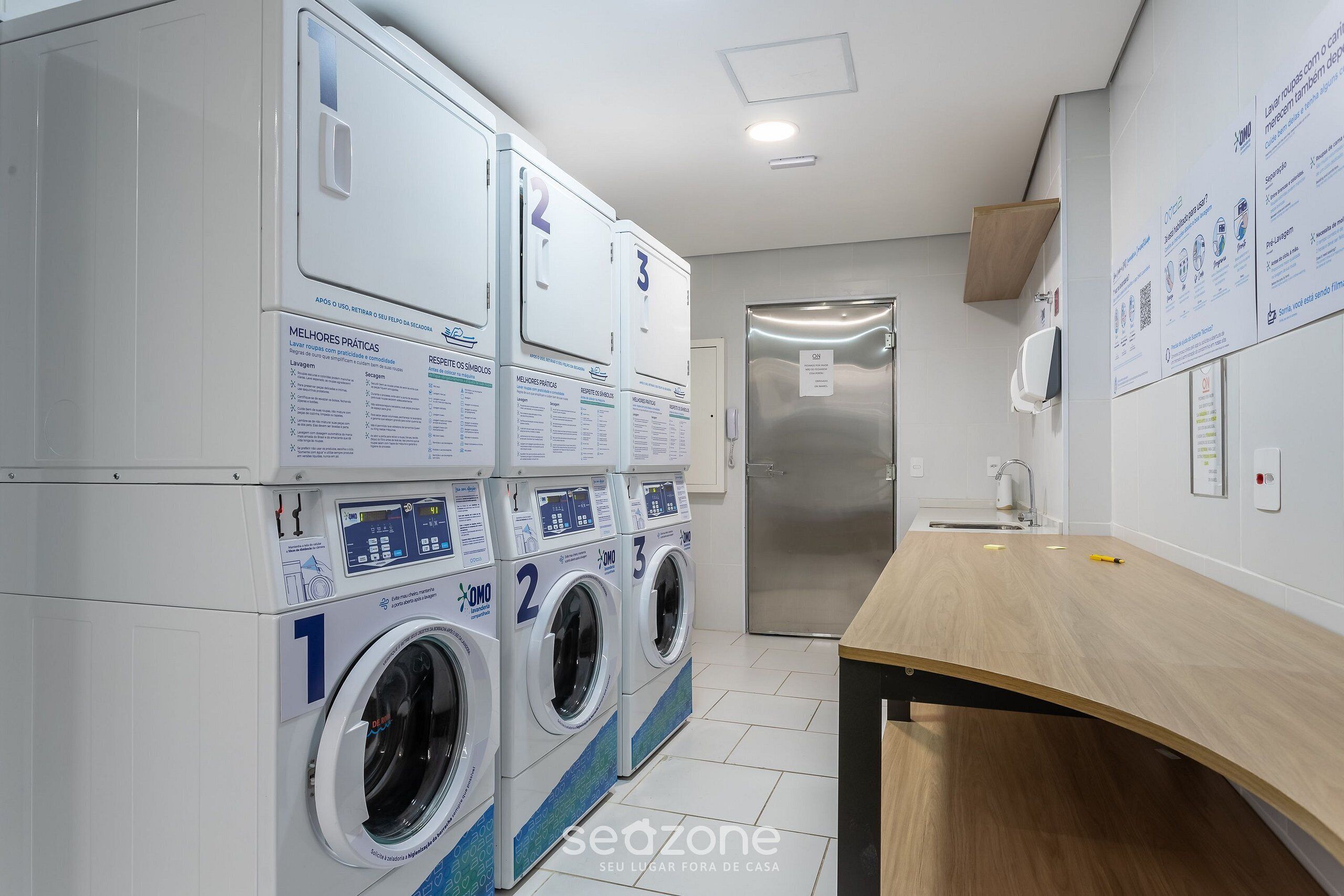 A laundry area with three washing machines, a sink, and a wooden counter.