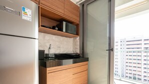 Une cuisine moderne équipée d’un réfrigérateur, d’un four à micro-ondes et d’une cuisinière encastrés. On trouve un meuble en bois au-dessus du plan de travail et une porte-fenêtre coulissante sur la droite.