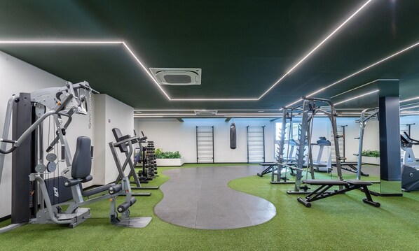 A modern gym with various exercise equipment, a green artificial turf floor, and a view of the city through large windows.