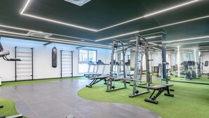Une salle de sport moderne équipée de divers appareils d’exercice, d’un sac de frappe et d’un espace recouvert d’un gazon synthétique vert.