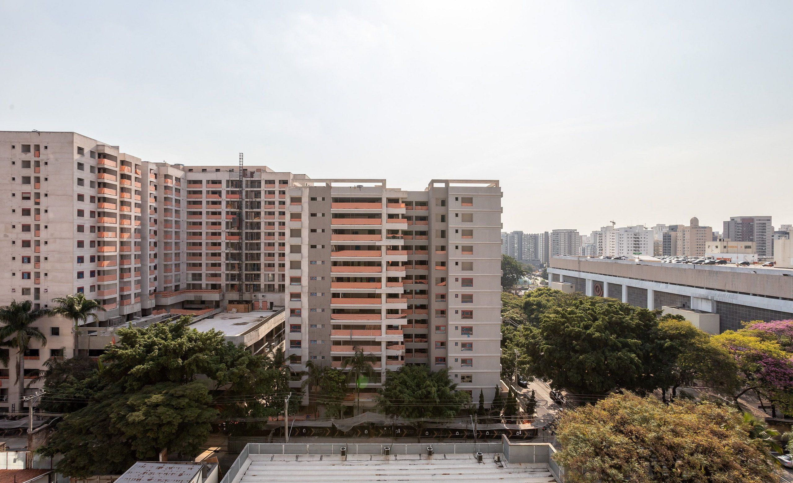 Un edificio residencial de varios pisos con balcones, rodeado de árboles y otros edificios.