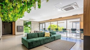 A modern lobby with a green sofa, a patterned rug, and a ceiling with a green plant installation.