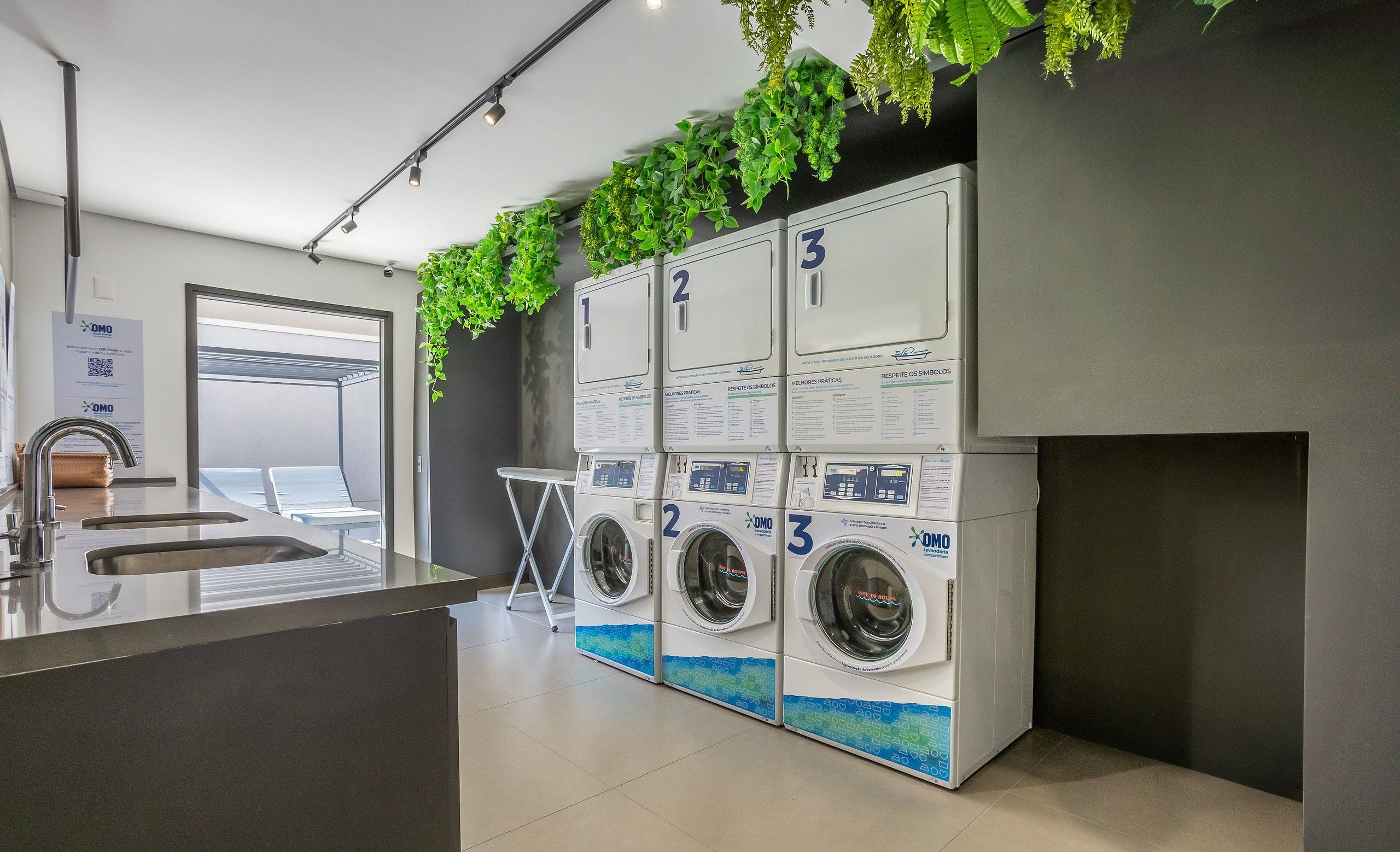 A modern laundry area with three washing machines, a sink, and a small table.