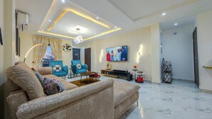 A modern living room with a sofa, two armchairs, a TV, and a decorative globe on the wall. - Elegant 2BR in Lekki Phase 1 • Steady Power, Pool, PS5 , Fast WiFi, Balconies (Lekki)