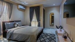 A modern hotel room with a large bed, air conditioning unit, curtains, a mirror, and a small table with a plant. - Elegant 2BR in Lekki Phase 1 • Steady Power, Pool, PS5 , Fast WiFi, Balconies (Lekki)