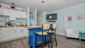 A kitchen with white cabinets, a blue island, and two bar stools.