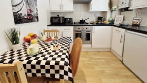 A compact kitchen with white cabinets, a black and white checkered tablecloth, and a painting of a bridge. - Stylish London FLAT near Highgate tube station (London)