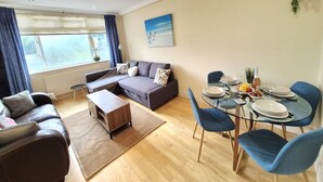 A modern living room with a sofa, coffee table, and dining area with chairs and a table set for two. - Stylish London FLAT near Highgate tube station (London)