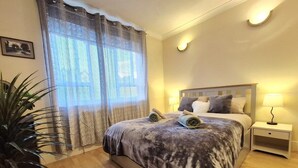 A bedroom with a large bed, bedside tables, a potted plant, and patterned curtains. - Stylish London FLAT near Highgate tube station (London)