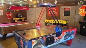 Ein Billardtisch, ein Kicker und eine Flipperkugelmaschine in einem Raum mit Graffiti und verschiedenen Schildern an den Wänden.
