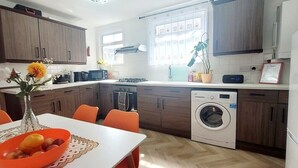 Moderni keittiö, jossa on puukalusteet, sisäänrakennettu pesukone sekä ruokailutila pöydän ja tuolien kera.