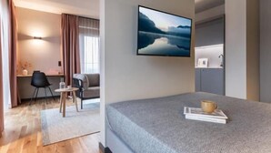 Une chambre d’hôtel moderne équipée d’un lit, d’un bureau, d’une chaise, d’un canapé et d’un tableau au mur.