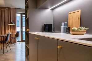 Una cocina moderna con horno integrado, una cafetera y un bol de verduras en la encimera.